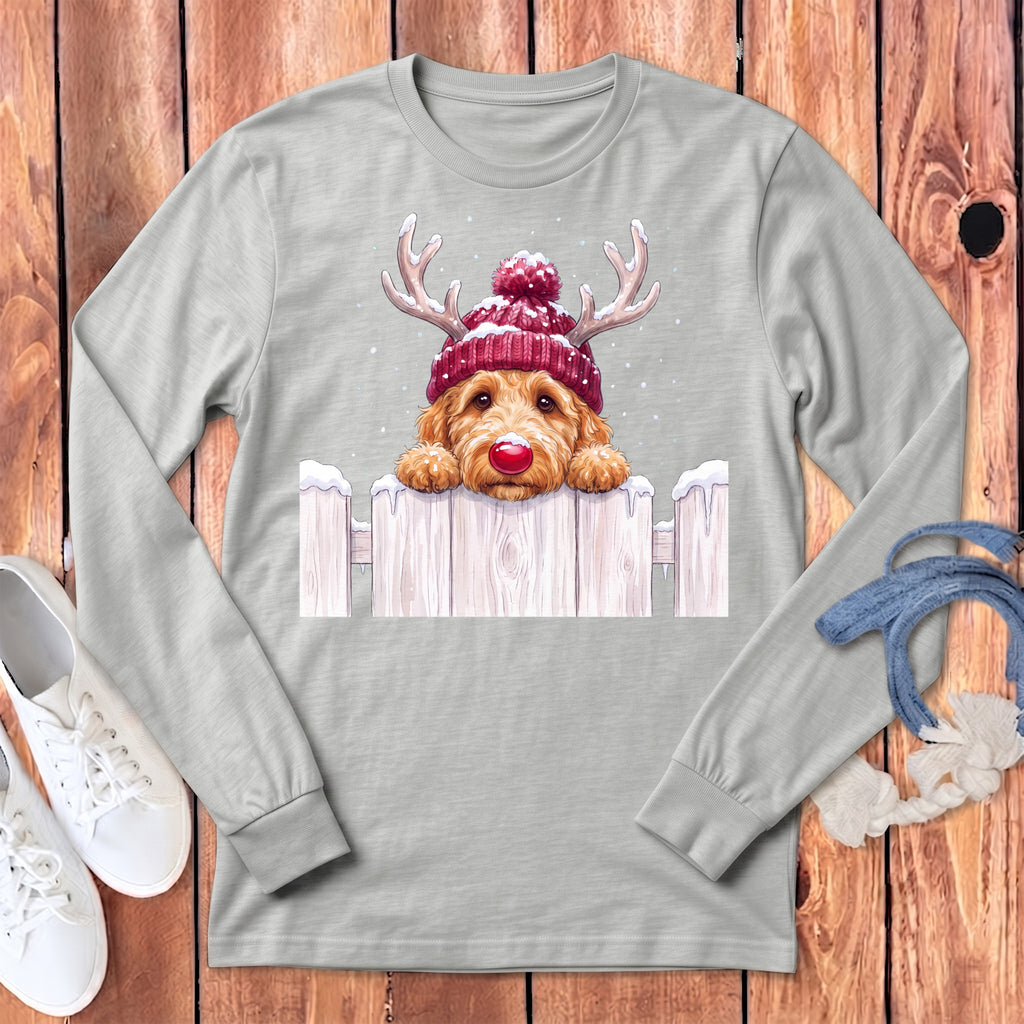 Goldendoodle wearing antlers and red hat peeking over a snowy fence.
