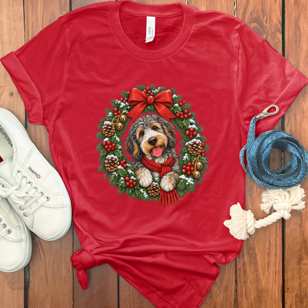 A red t-shirt features a graphic of a labradoodle wearing a red scarf inside a Christmas wreath.
