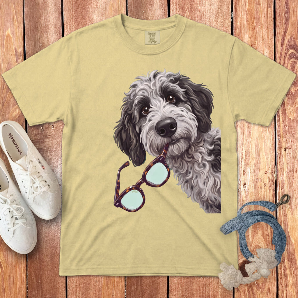Yellow t-shirt featuring an illustrated gray doodle dog holding tortoiseshell glasses in its mouth.