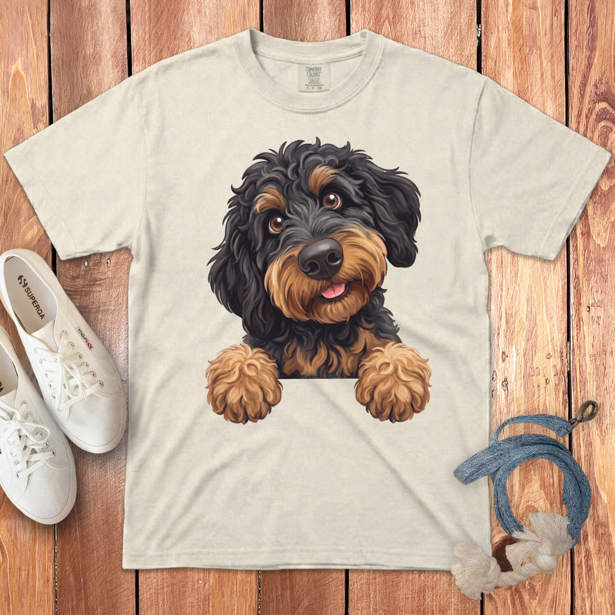 Cream t-shirt with black and tan doodle dog graphic, white sneakers, and rope toy.