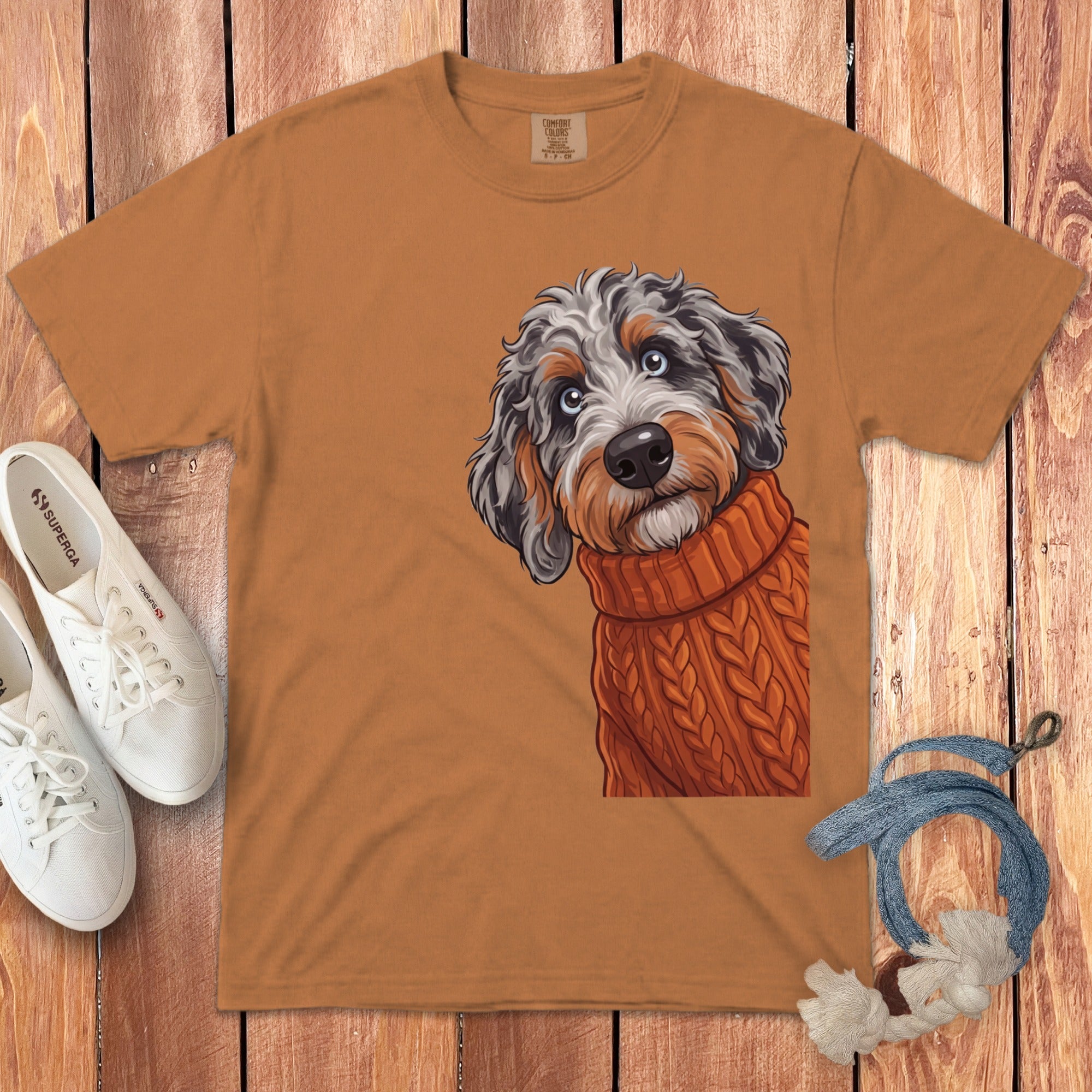 Orange t-shirt graphic of a doodle dog wearing a knitted sweater.