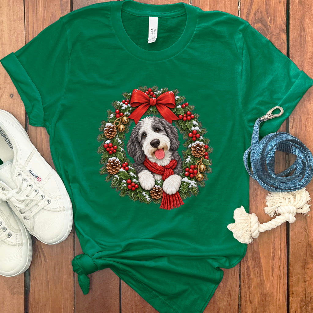 Kelly green short-sleeve t-shirt featuring a Christmas wreath graphic with a doodle dog wearing a red scarf.