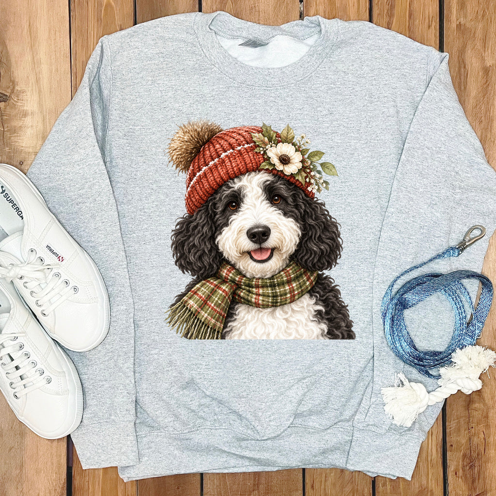 Grey sweatshirt with illustration of dog wearing a beanie and scarf, next to white sneakers.