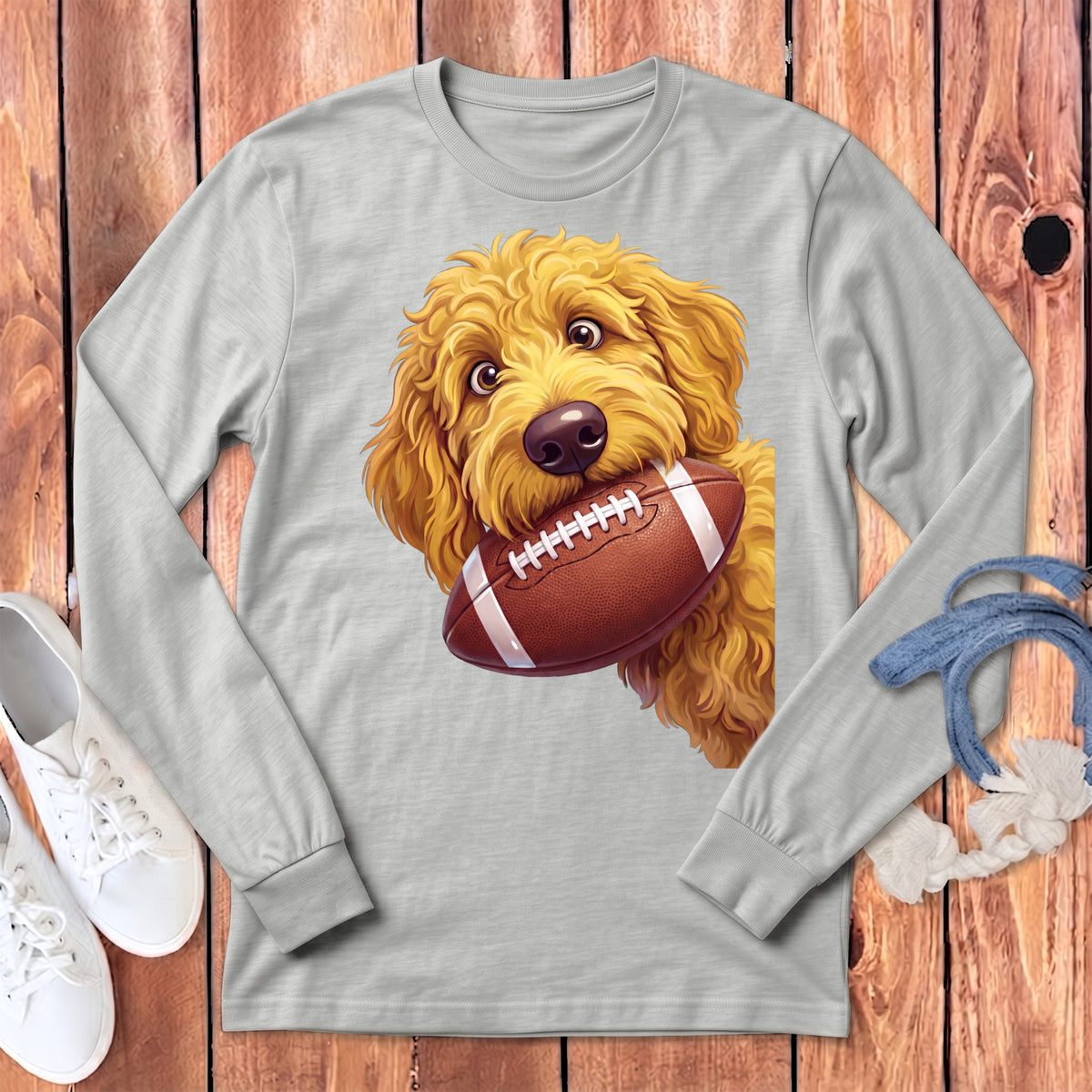 Goldendoodle puppy holding a football in its mouth on a gray long-sleeve shirt.