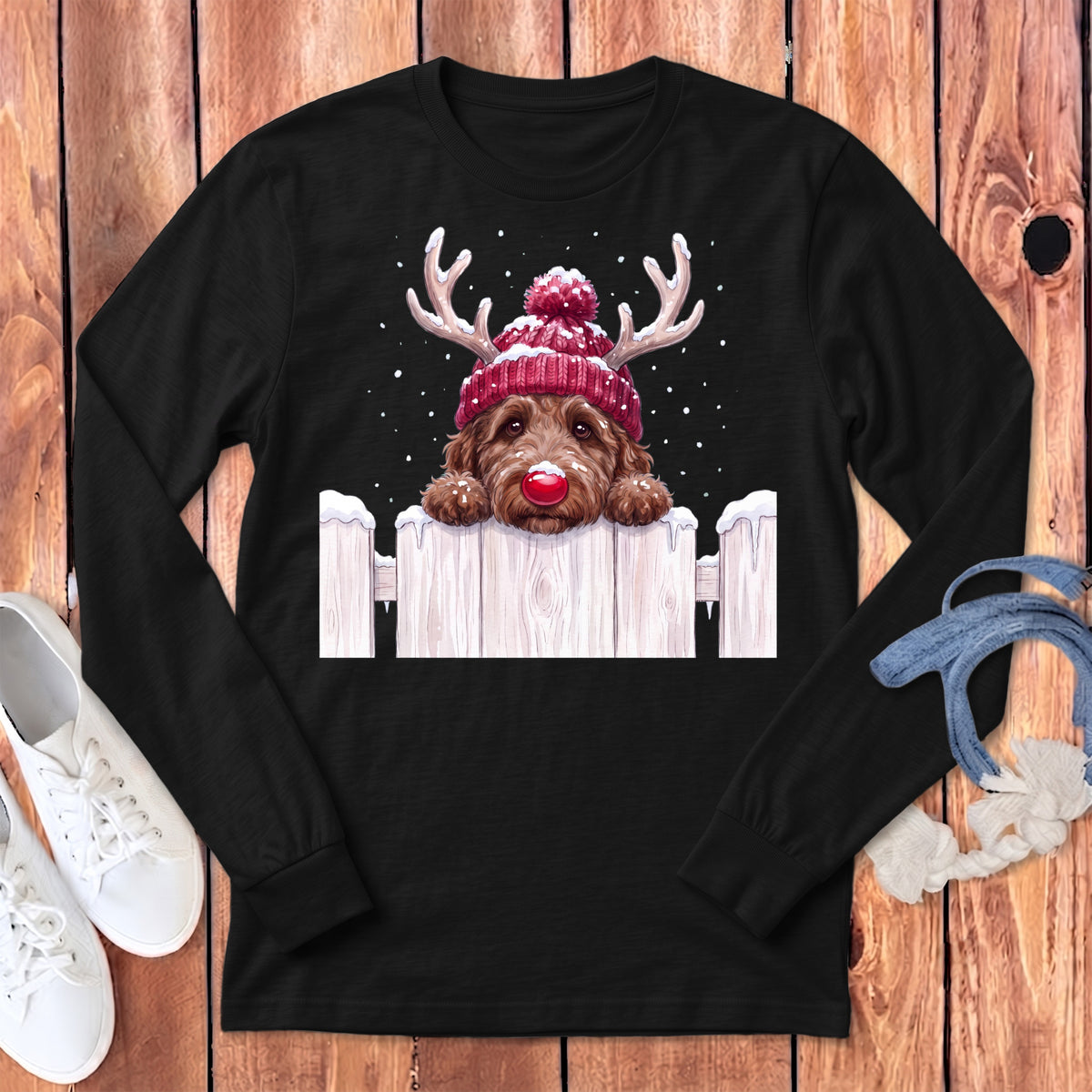Brown dog wearing a Santa hat and antlers peeking over a snowy fence.