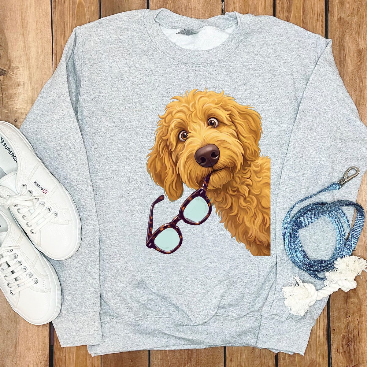 A gray crewneck sweatshirt featuring a cartoon golden doodle dog holding tortoiseshell glasses in its mouth.