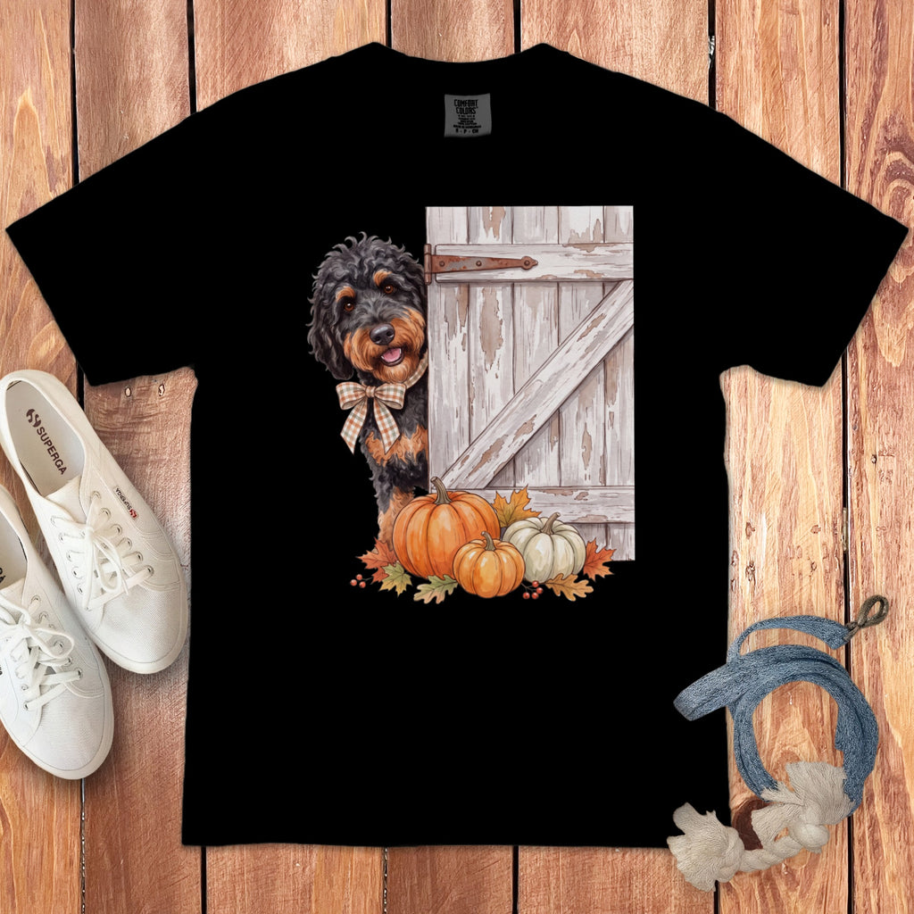 Black t-shirt with a dog peeking from behind a rustic door with pumpkins.