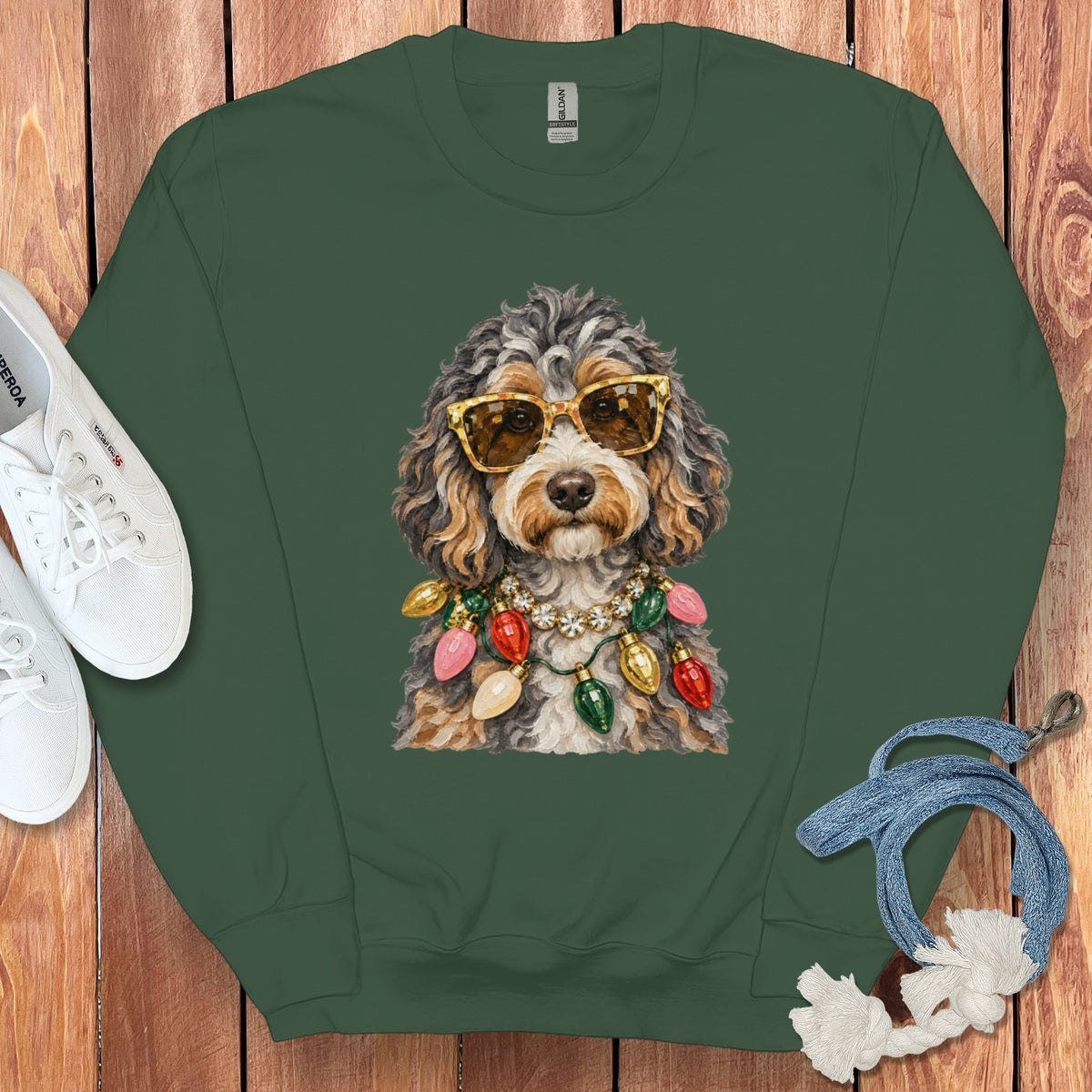 Dog wearing sunglasses and Christmas lights necklace on a green sweatshirt.