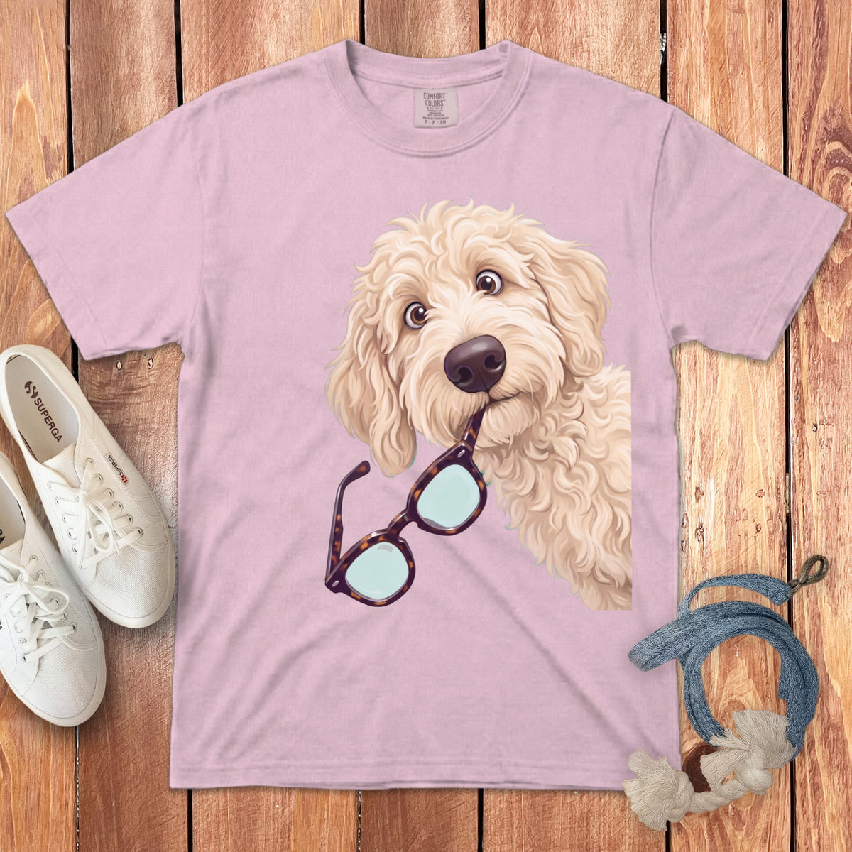 Light pink t-shirt featuring an illustration of a fluffy golden dog holding glasses in its mouth.