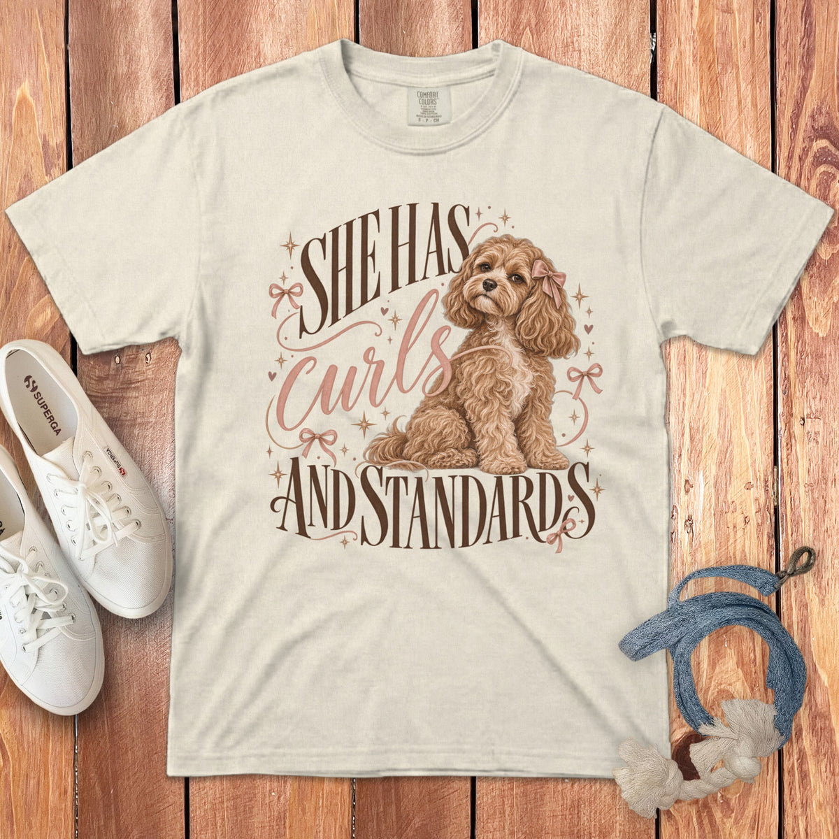 Off-white t-shirt featuring a graphic of a curly poodle and the text She Has Curls And Standards.