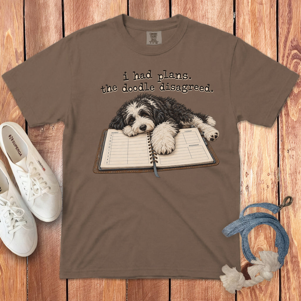 Brown t-shirt featuring a black and white doodle resting on a planner with text reading, i had plans. the doodle disagreed.