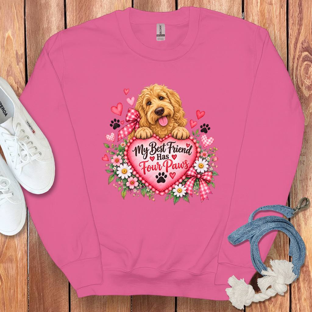 A pink crewneck sweatshirt featuring a graphic of a golden puppy resting on a heart with flowers, surrounded by white sneakers and a blue leash on a wooden background.