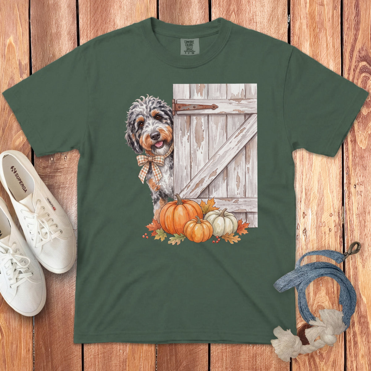 Green t-shirt featuring a dog peeking from behind a rustic door with pumpkins and leaves.