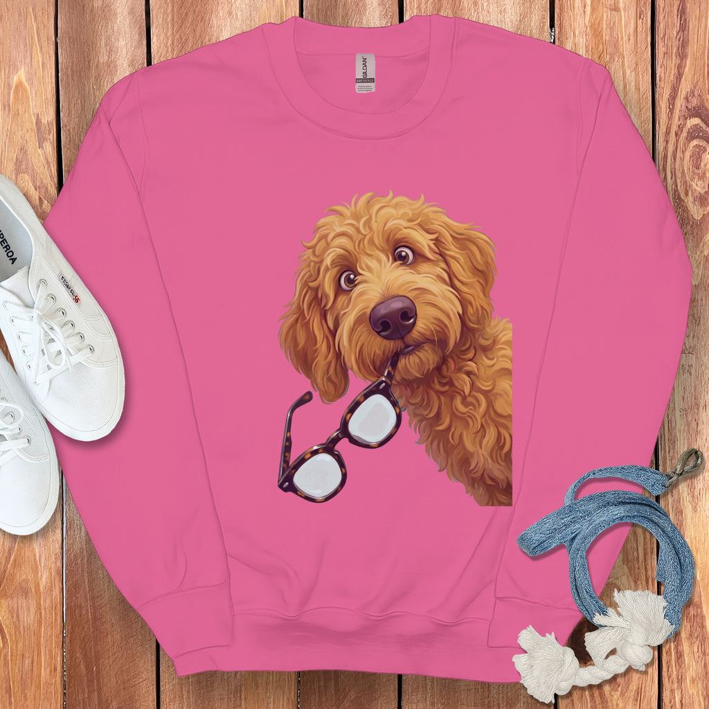 A pink crewneck sweatshirt with a graphic of a golden doodle dog holding glasses in its mouth.