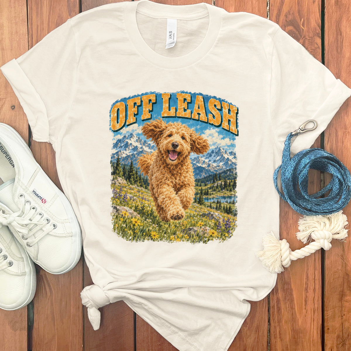 T-shirt graphic with a golden doodle running in a mountain meadow under "OFF LEASH" text.