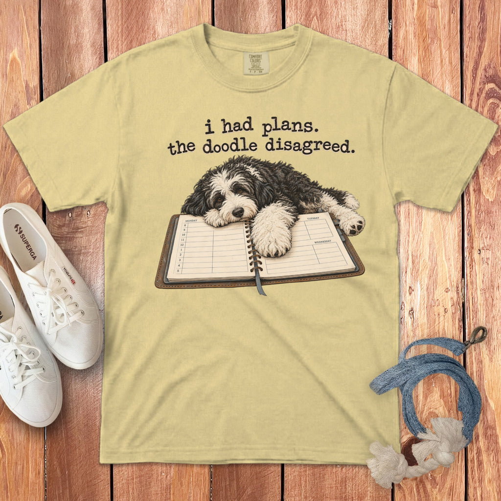 A yellow t-shirt features a doodle dog resting on an open planner and text reading i had plans the doodle disagreed.
