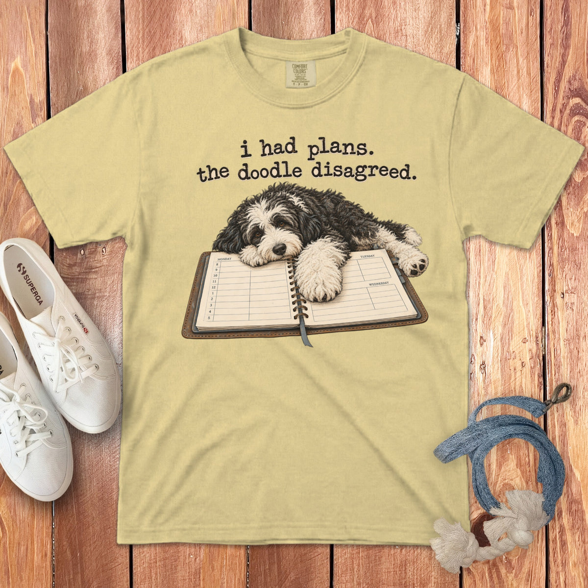 A yellow t-shirt features a doodle dog resting on an open planner and text reading i had plans the doodle disagreed.