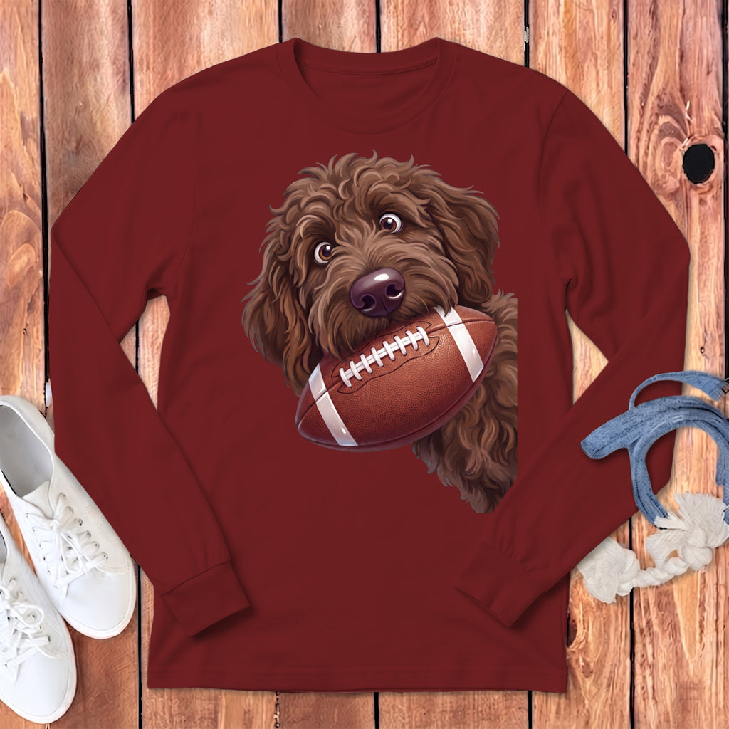 Brown doodle dog holding a football on a maroon long-sleeve shirt.