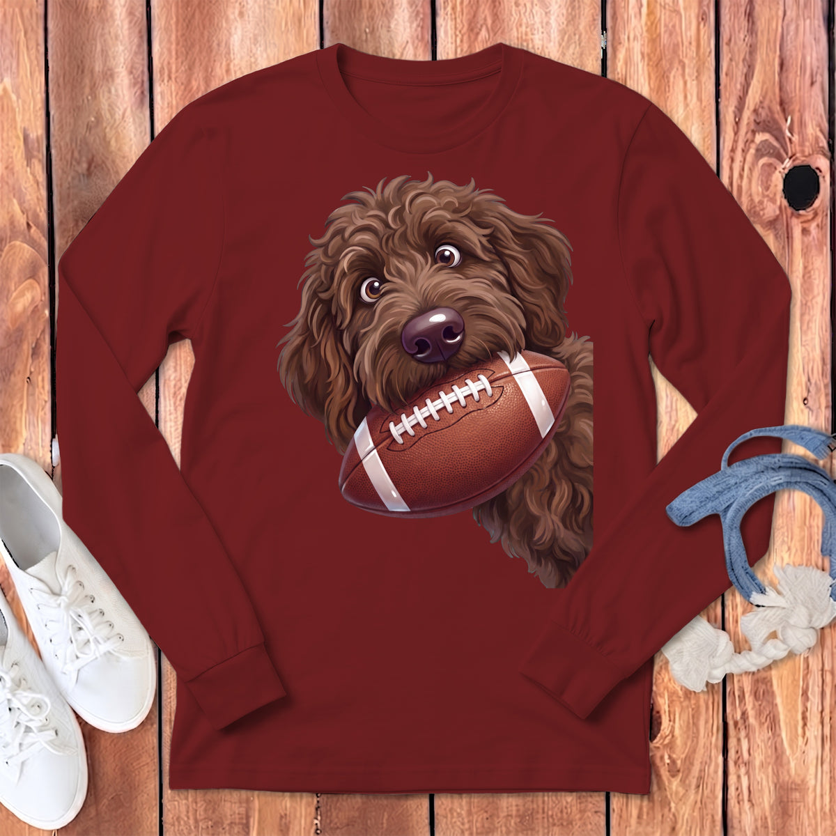 Brown doodle dog holding a football on a maroon long-sleeve shirt.
