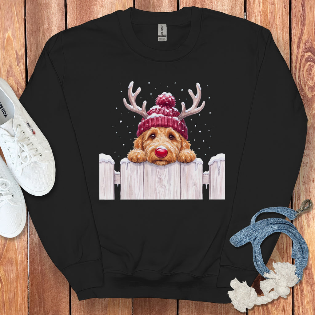Black crewneck sweatshirt featuring a graphic of a golden doodle with reindeer antlers, a red beanie, and a red nose peeking over a snow-covered wooden fence.