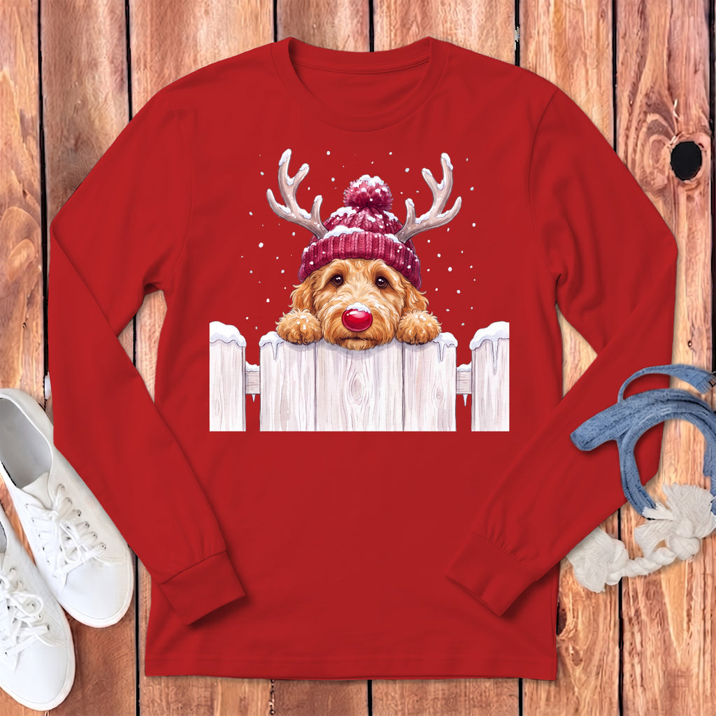 Golden doodle wearing a Santa hat and antlers peeking over a snowy fence.