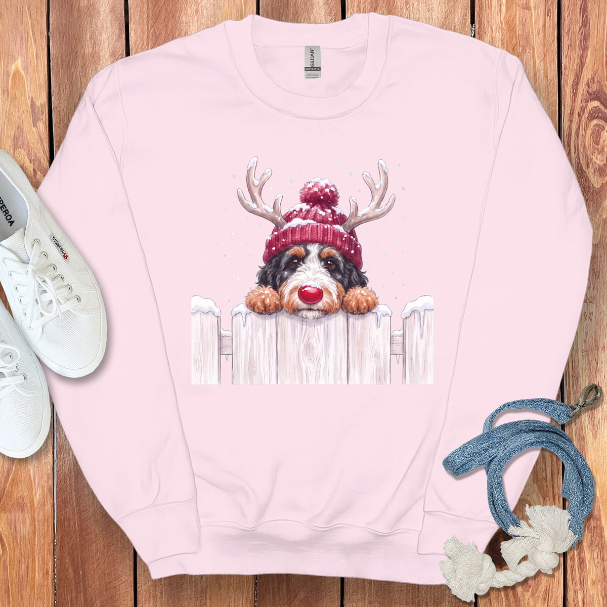 Pink sweatshirt featuring a watercolor dog in a Santa hat and antlers over a fence.