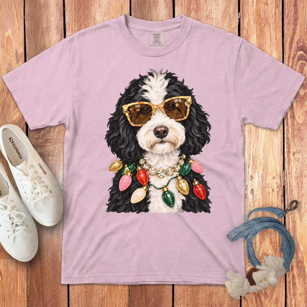 Bernedoodle wearing sunglasses and festive Christmas lights necklace on pink t-shirt.