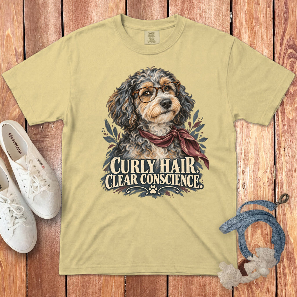 A pale yellow t-shirt features a graphic of a fluffy dog wearing glasses and a scarf, accompanied by the text "Curly Hair Clear Conscience."