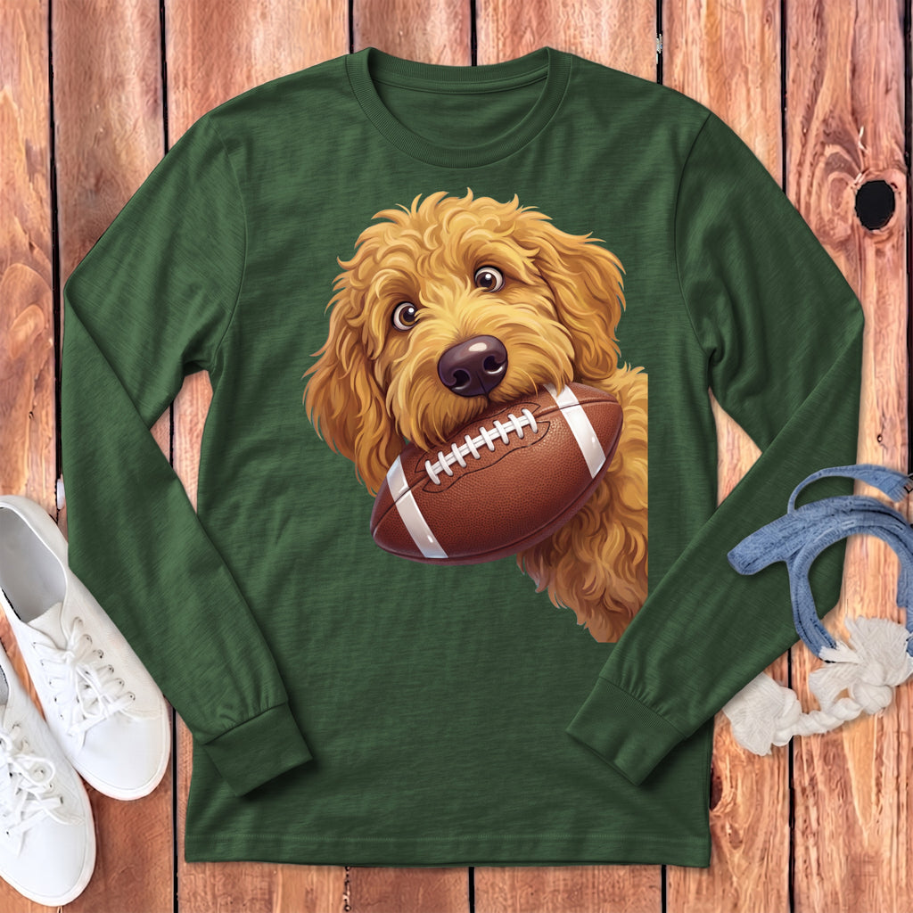 Goldendoodle puppy with football in mouth on a green long-sleeve shirt.