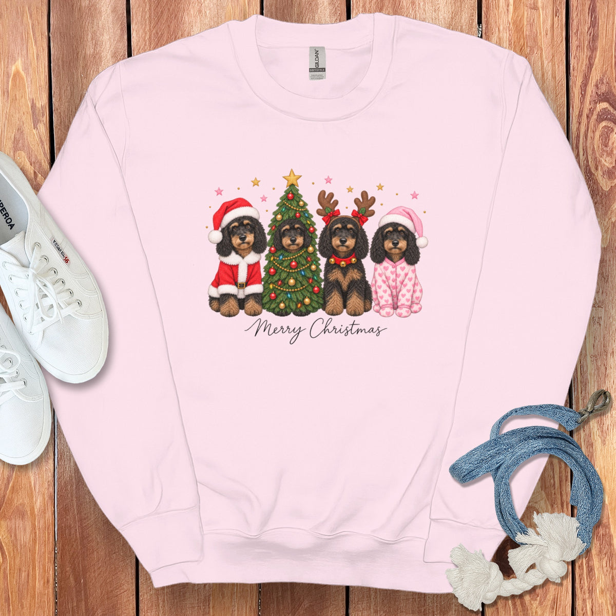 A light pink crewneck sweatshirt features a graphic of four dogs in Christmas costumes around a decorated tree, with Merry Christmas text below.