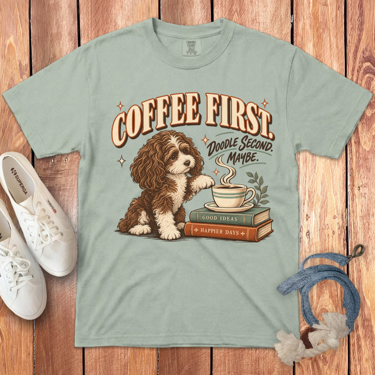 Sage green t-shirt featuring a doodle dog next to books and a coffee cup with text.