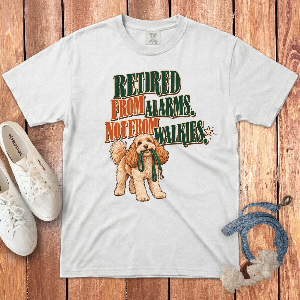 A white t-shirt featuring a graphic of a curly-haired dog holding a leash and text reading Retired From Alarms, Not From Walkies.