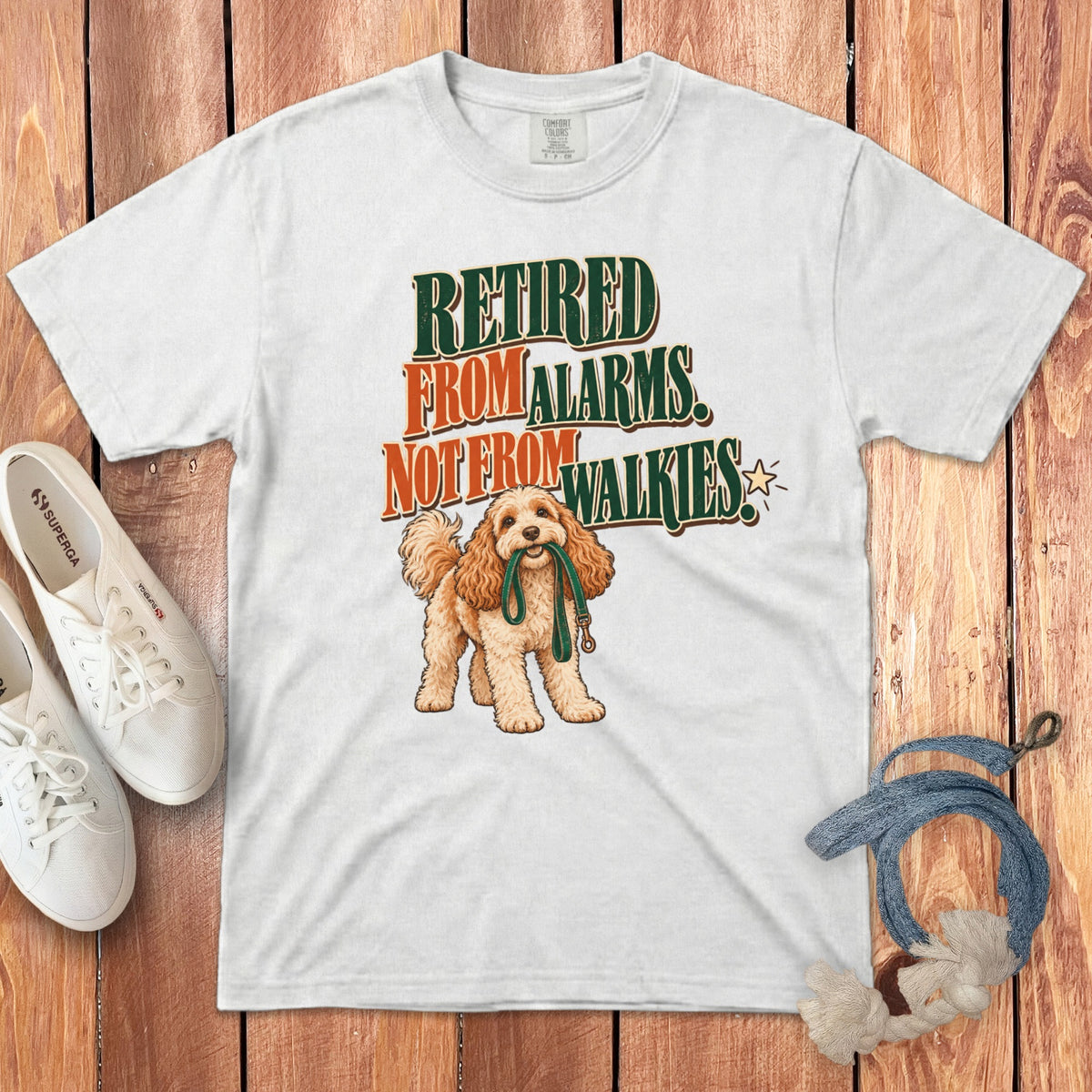 A white t-shirt featuring a graphic of a curly-haired dog holding a leash and text reading Retired From Alarms, Not From Walkies.