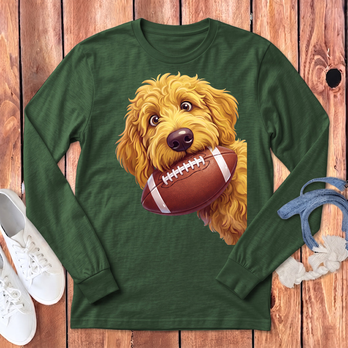 Goldendoodle dog holding a football in its mouth on a green long-sleeve shirt.