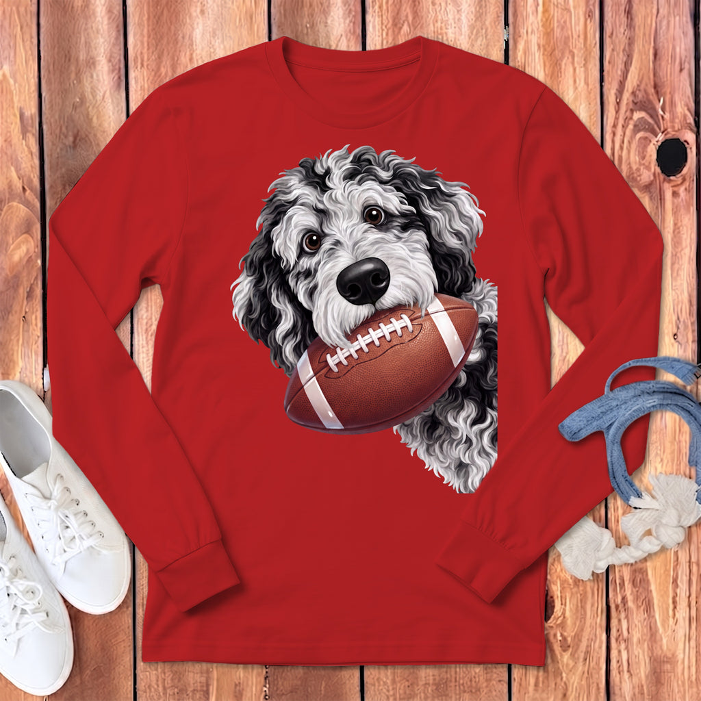 A red long-sleeve t-shirt with a black and white doodle dog holding a football in its mouth.