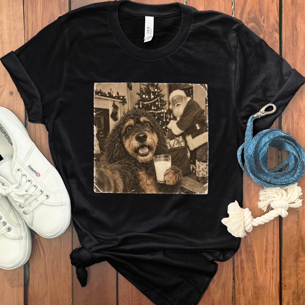 A black t-shirt printed with a vintage-style graphic of a dog holding a glass of milk next to Santa Claus.