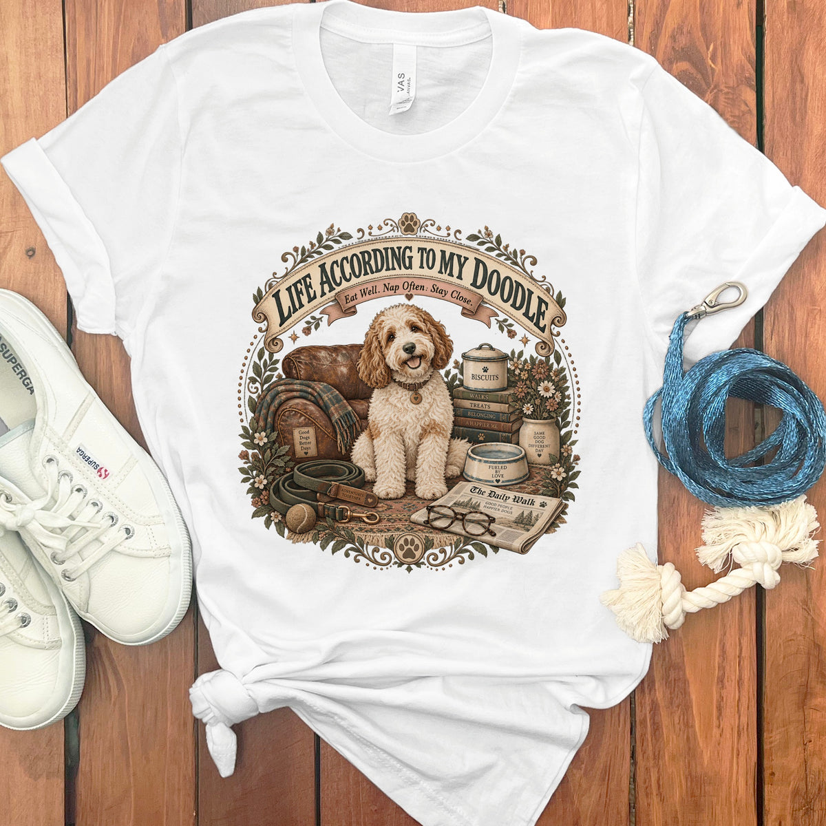 White t-shirt graphic with a doodle dog sitting amongst books and dog accessories.
