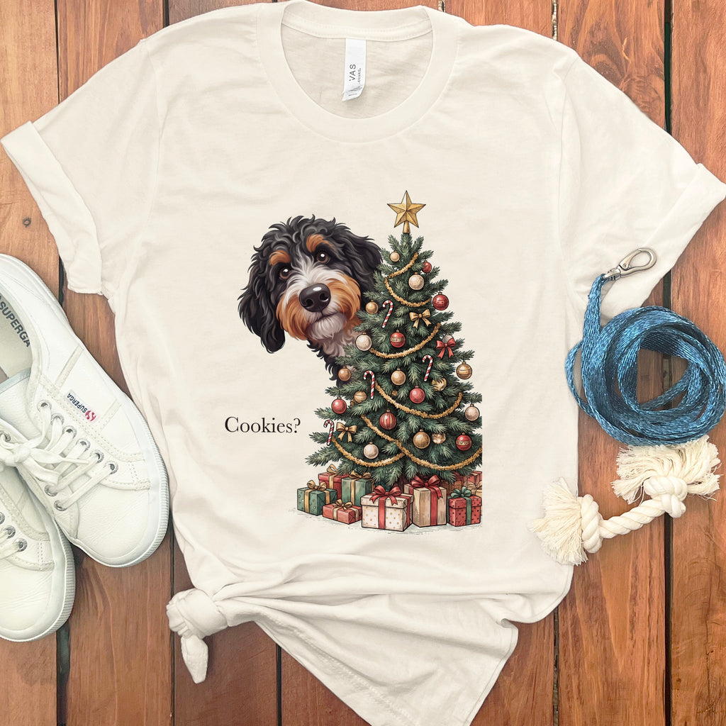 Bernedoodle peeking from behind a decorated Christmas tree with gifts and the text "Cookies?".