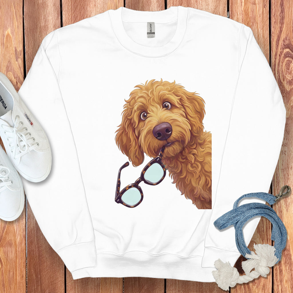A white crewneck sweatshirt features an illustrated golden doodle dog holding tortoiseshell glasses in its mouth.