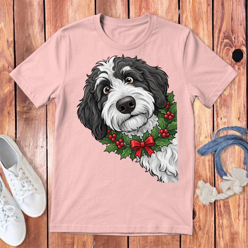 Black and white dog with holly wreath and red bow on pink t-shirt.