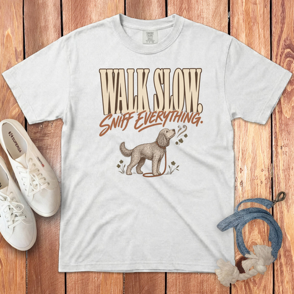 White t-shirt with a vintage dog illustration and text that reads Walk Slow Sniff Everything on a wooden background.