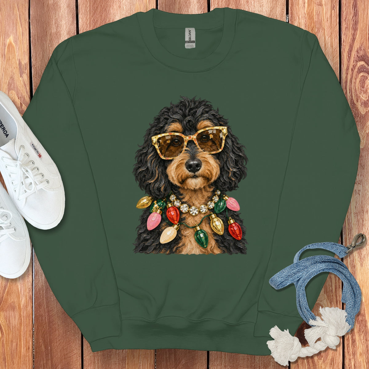 Dog wearing sunglasses and Christmas lights necklace on green sweatshirt.