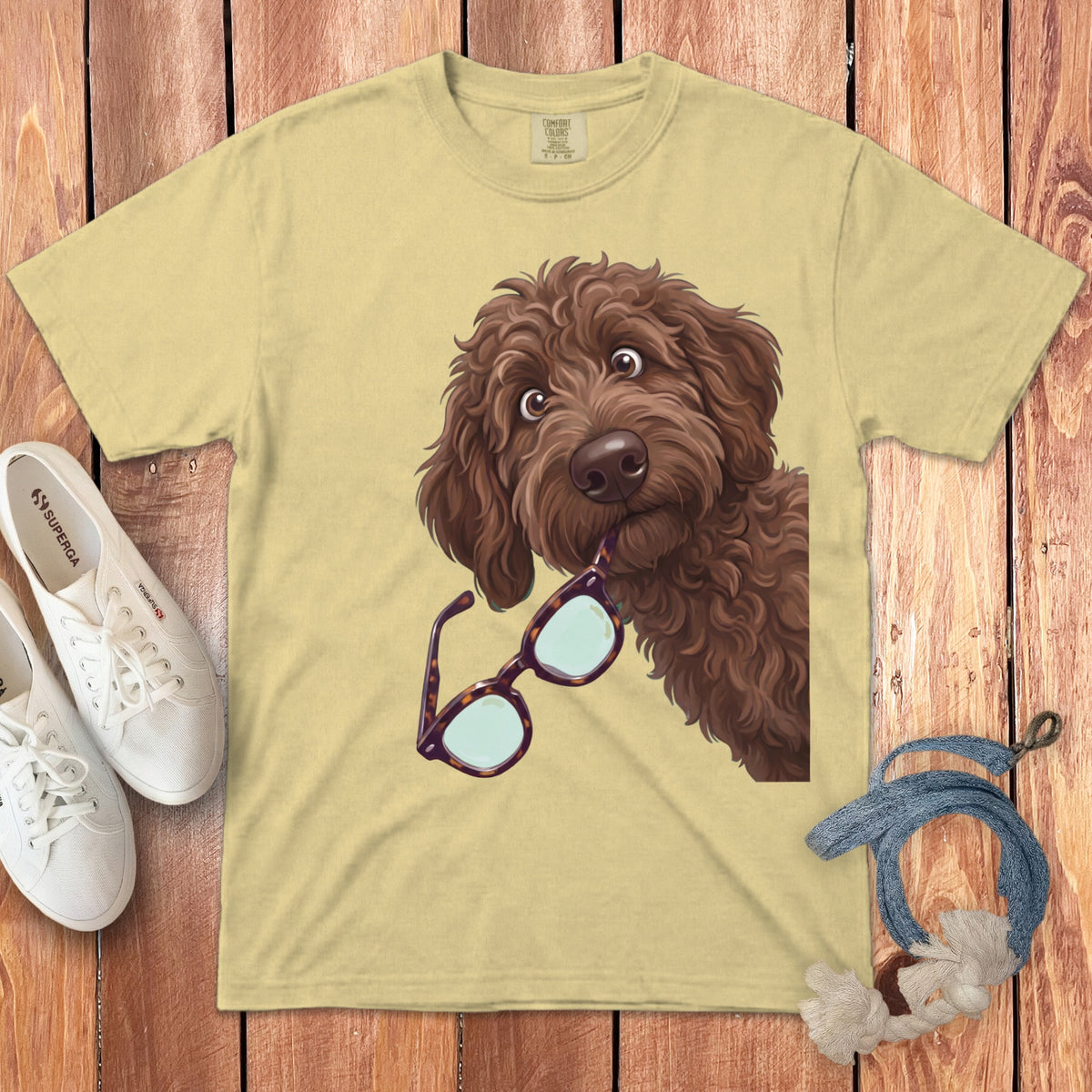 Pale yellow t-shirt featuring a cartoon doodle dog holding tortoiseshell glasses in its mouth.