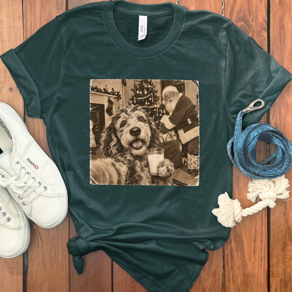 A dark green t-shirt featuring a sepia-toned graphic of a fluffy dog holding a glass of milk in front of Santa Claus.