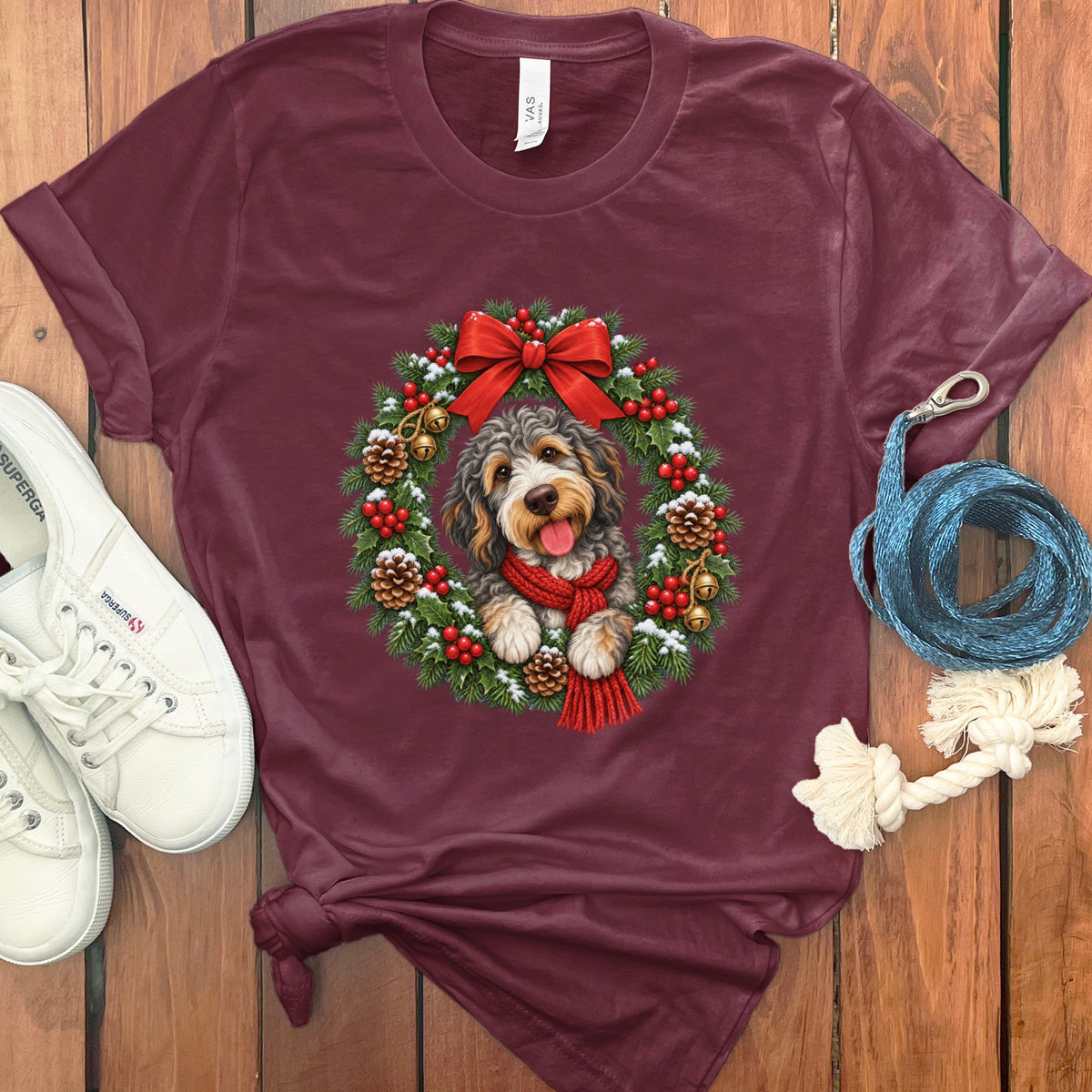 Maroon t-shirt featuring a doodle dog wearing a red scarf inside a Christmas wreath graphic.