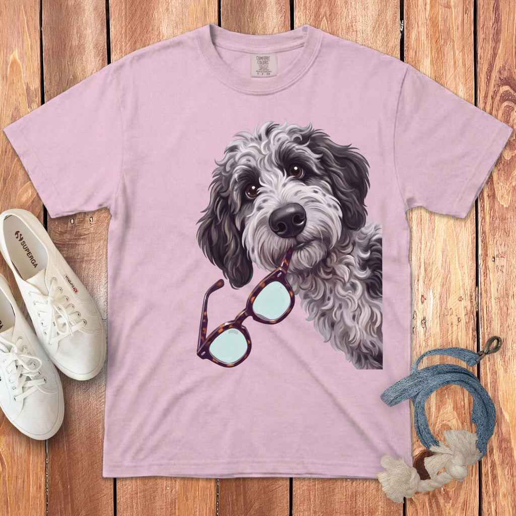 Light pink t-shirt featuring an illustration of a doodle dog holding glasses, laid on a wooden background.