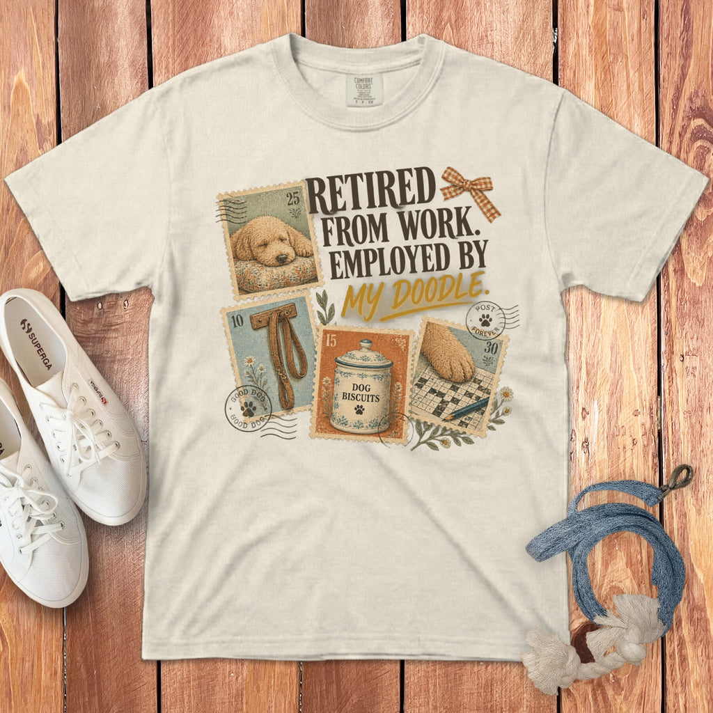 Light-colored t-shirt featuring vintage postage stamp graphics of a doodle dog, treats, and text reading Retired From Work Employed By My Doodle.
