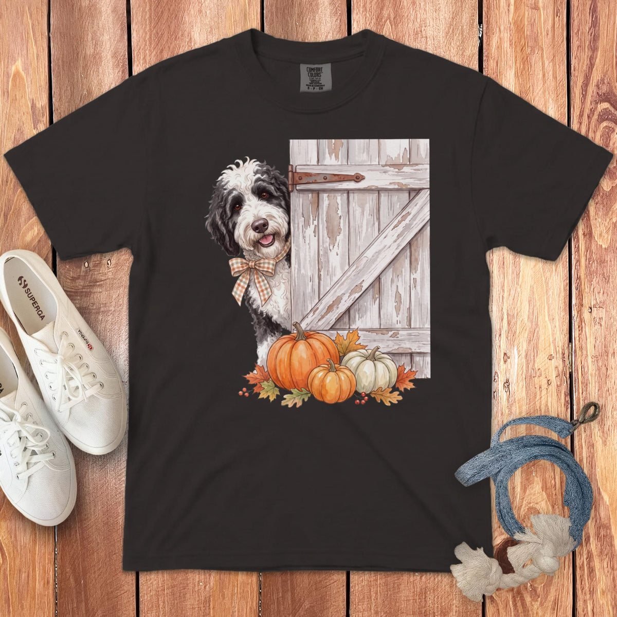 Black t-shirt with dog peeking from behind rustic wooden door and pumpkins.