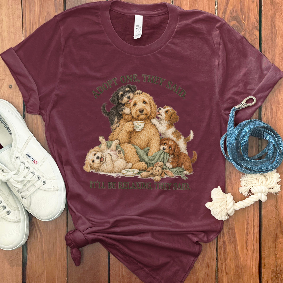 Maroon t-shirt with illustration of a family of dogs and text "Adopt One, They Said."