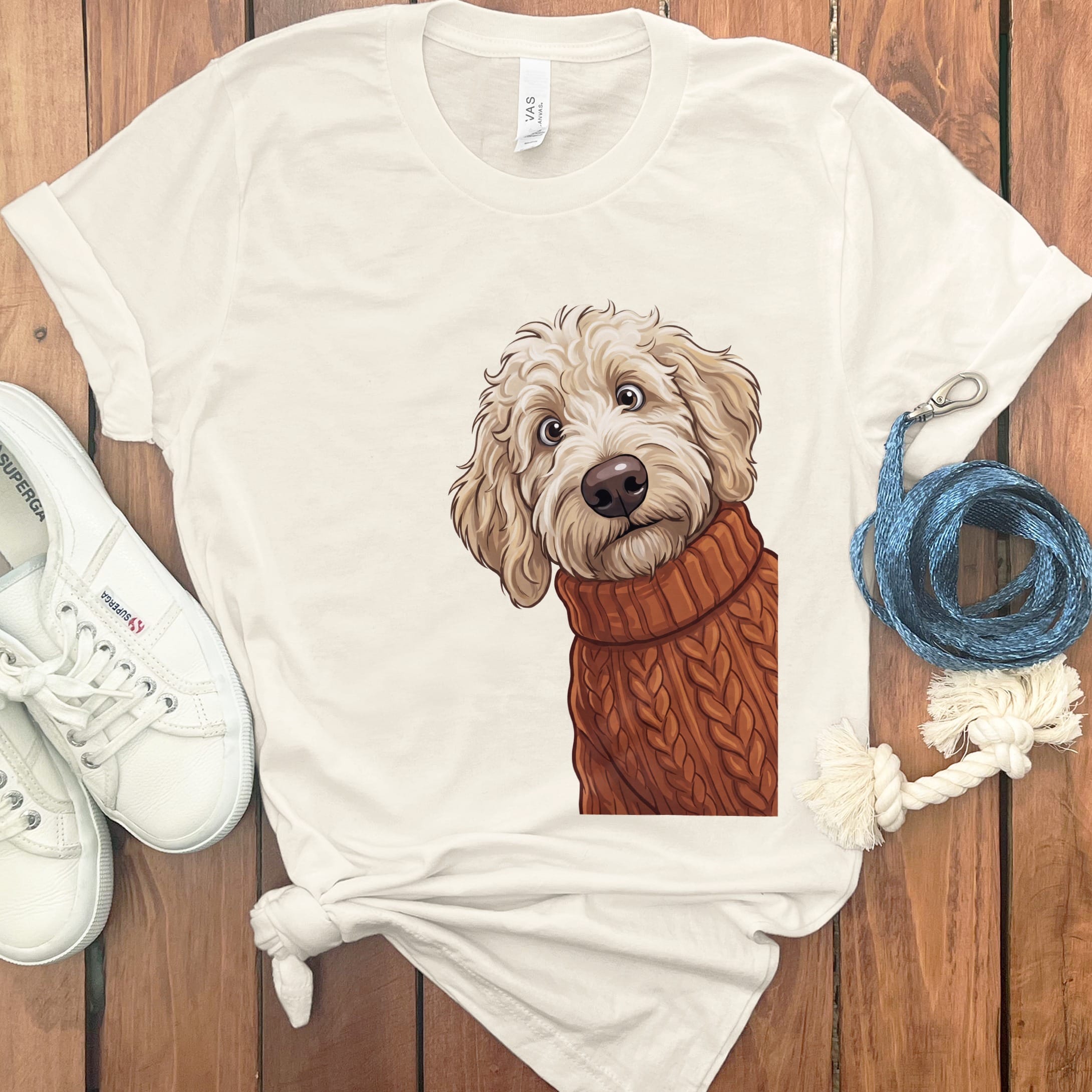 Cream t-shirt with a drawing of a fluffy dog wearing a brown cable-knit sweater.